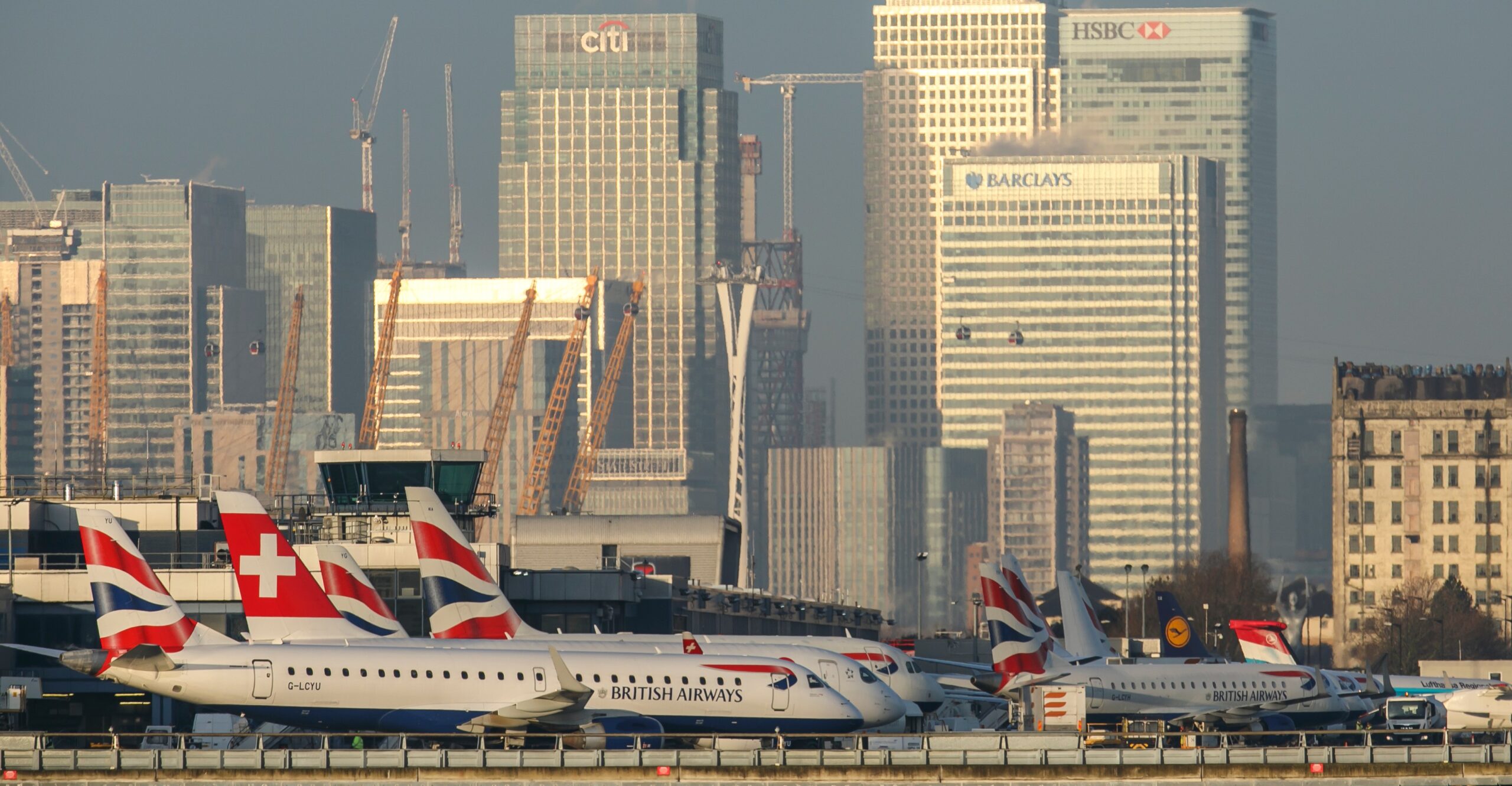 Aircraft stationed at the London City Airport. Office buildings in the background.