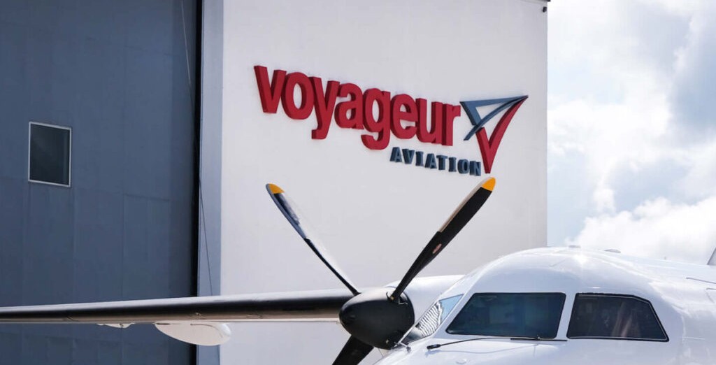 Outside of building, sign reads "Voyageur Aviation", plane at the bottom of the screen.