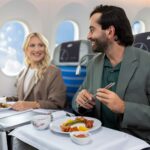 Passengers seated in LOT Polish Airlines Business Class enjoying a plated meal during a long-haul flight.