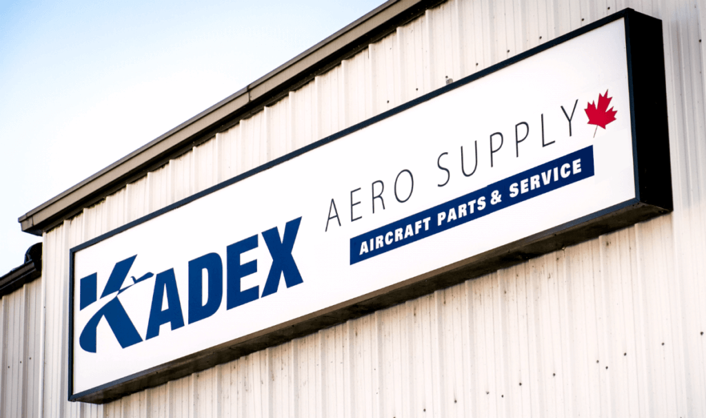 Sign on the side of a building, reads "Kadex Aero Supply aircraft parts & services".