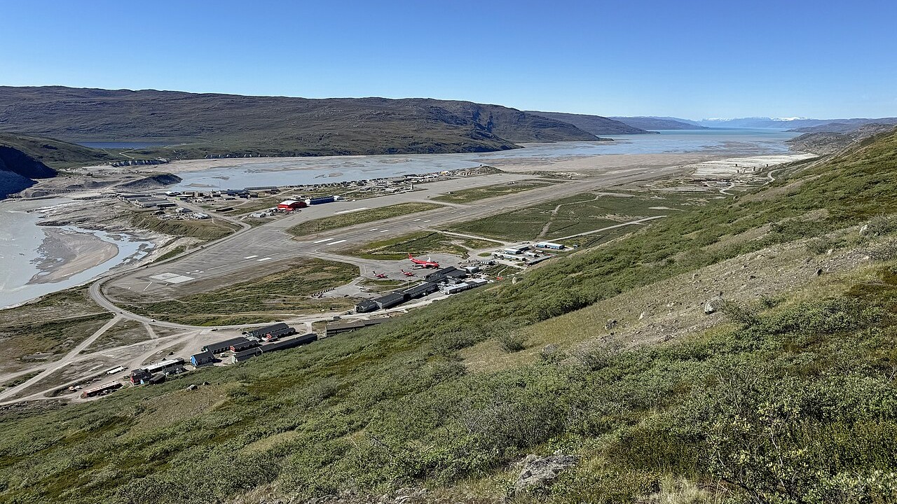 Kangerlussuaq Airport, hills in foreground and blue sky and water in background.
