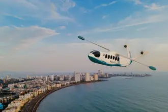 Mehair aircraft flying over the sea with a city in the left background.