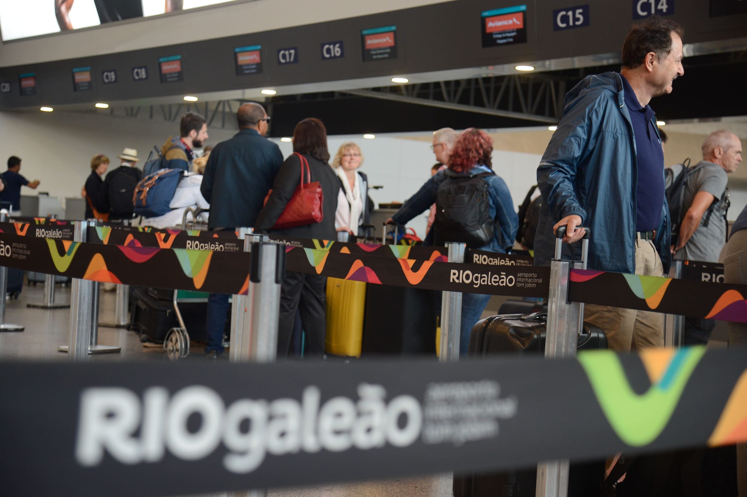 RIOgaleão banner at an airport terminal with passengers in the background.