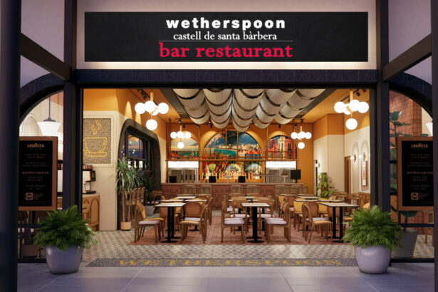 The storefront of the "Castell de Santa Bàrbera" pub, the first JD Wetherspoon location in mainland Europe, situated in the airside departures area of Alicante-Elche Miguel Hernández Airport. The entrance features a large blue sign with the pub's name in white lettering, located next to an airport restroom and opposite gate B30.