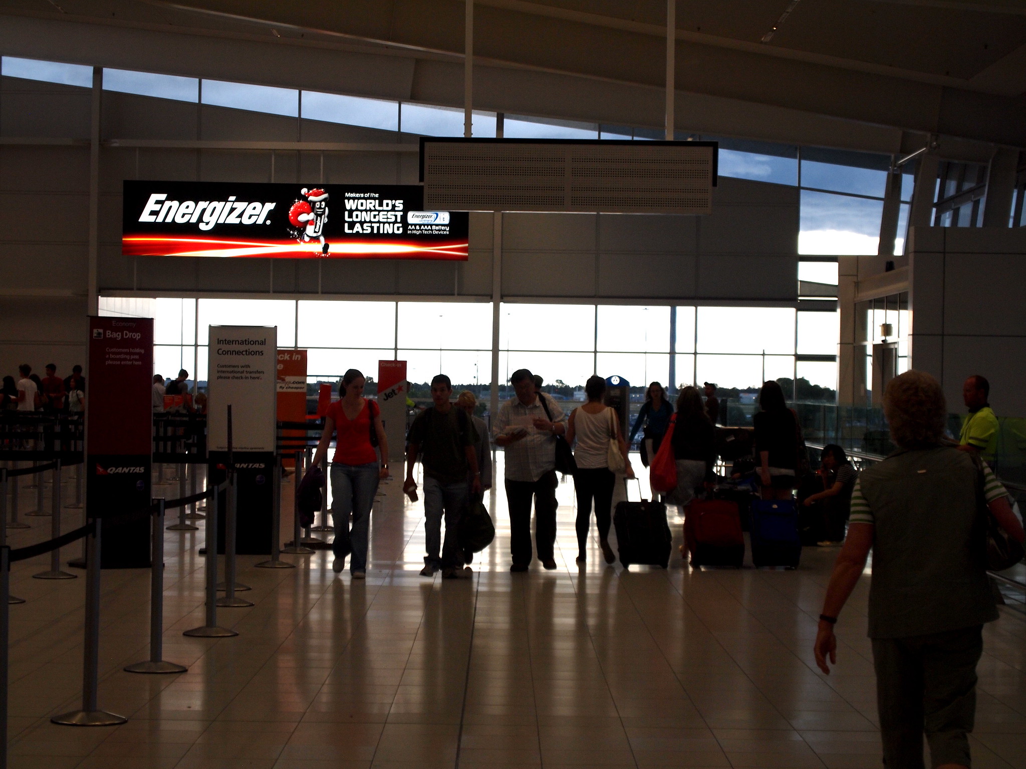 People walking through Adelaide Airport with suitcases and bags in hand, near Bag Drop queue.