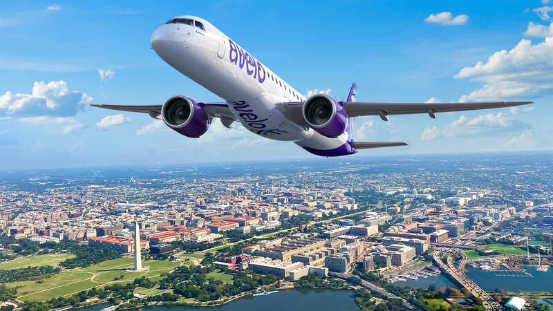 Avelo Airlines Embraer aircraft flying over the city, blue sky.