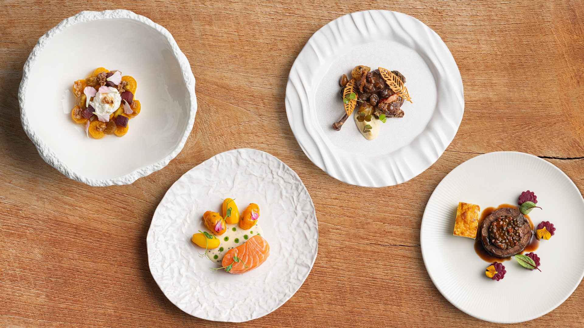 A selection of Michelin-starred dishes plated on white crockery, photographed from above on a wooden table.