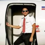 Fabio Espinal Nunez wearing sunglasses and posing in an aircraft doorway with a Dominican Republic flag displayed behind him.