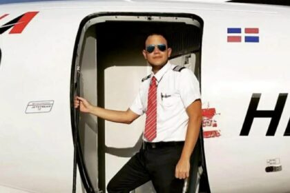 Fabio Espinal Nunez wearing sunglasses and posing in an aircraft doorway with a Dominican Republic flag displayed behind him.