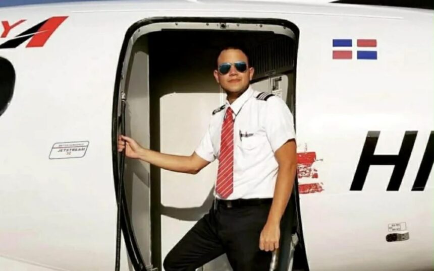 Fabio Espinal Nunez wearing sunglasses and posing in an aircraft doorway with a Dominican Republic flag displayed behind him.