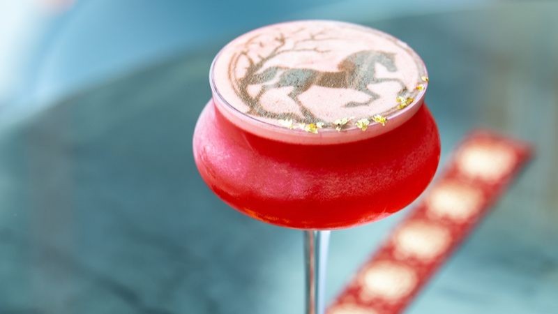 A red cocktail with a Horse image on the foam.