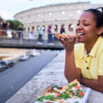 Woman eating a slice of pizza in front of the Colosseum