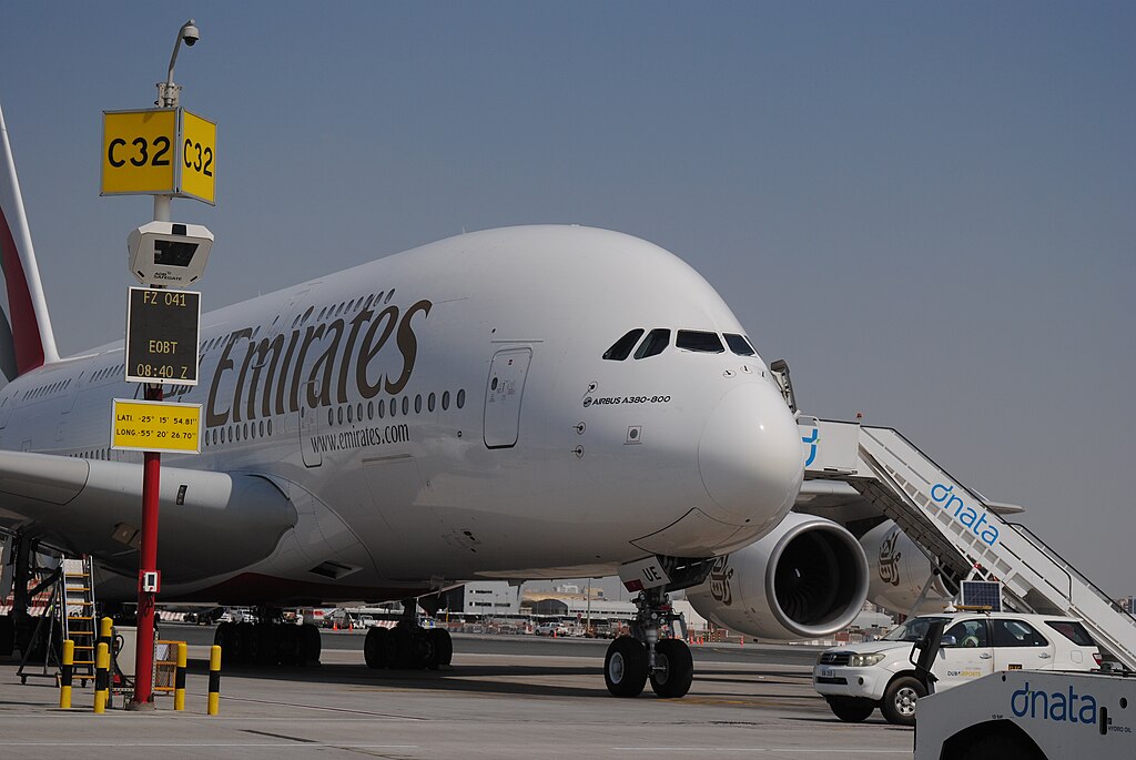 Emirates Airbus parked at Dubai International Airport. Ground vehicle parked beneath the aircraft, and a sign visible on the left side reading "C32".