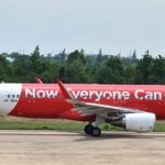 An AirAsia A320(SL) on the ground in front of trees and a blue sky