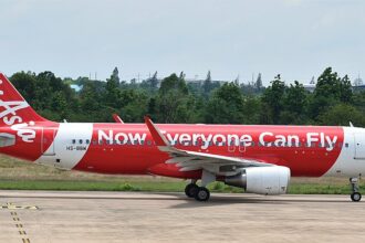 An AirAsia A320(SL) on the ground in front of trees and a blue sky
