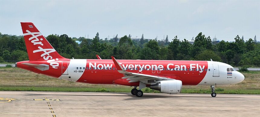 An AirAsia A320(SL) on the ground in front of trees and a blue sky