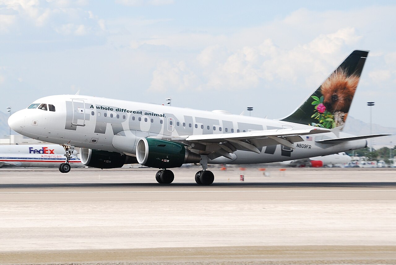 A Frontier Airlines jet rolls along a runway during landing, its wheels touching down on a wide concrete surface.