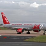 A silver and red commercial jetliner from Jet2 is taxiing on an airport runway under a cloudy sky.