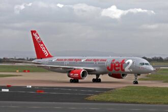 A silver and red commercial jetliner from Jet2 is taxiing on an airport runway under a cloudy sky.