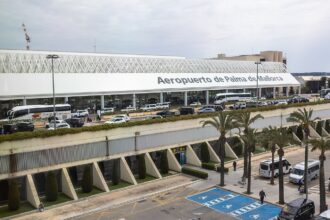 A wide view of a modern airport terminal labeled “Aeropuerto de Palma de Mallorca,” featuring a long white facade topped with a curved, lattice-like roof.