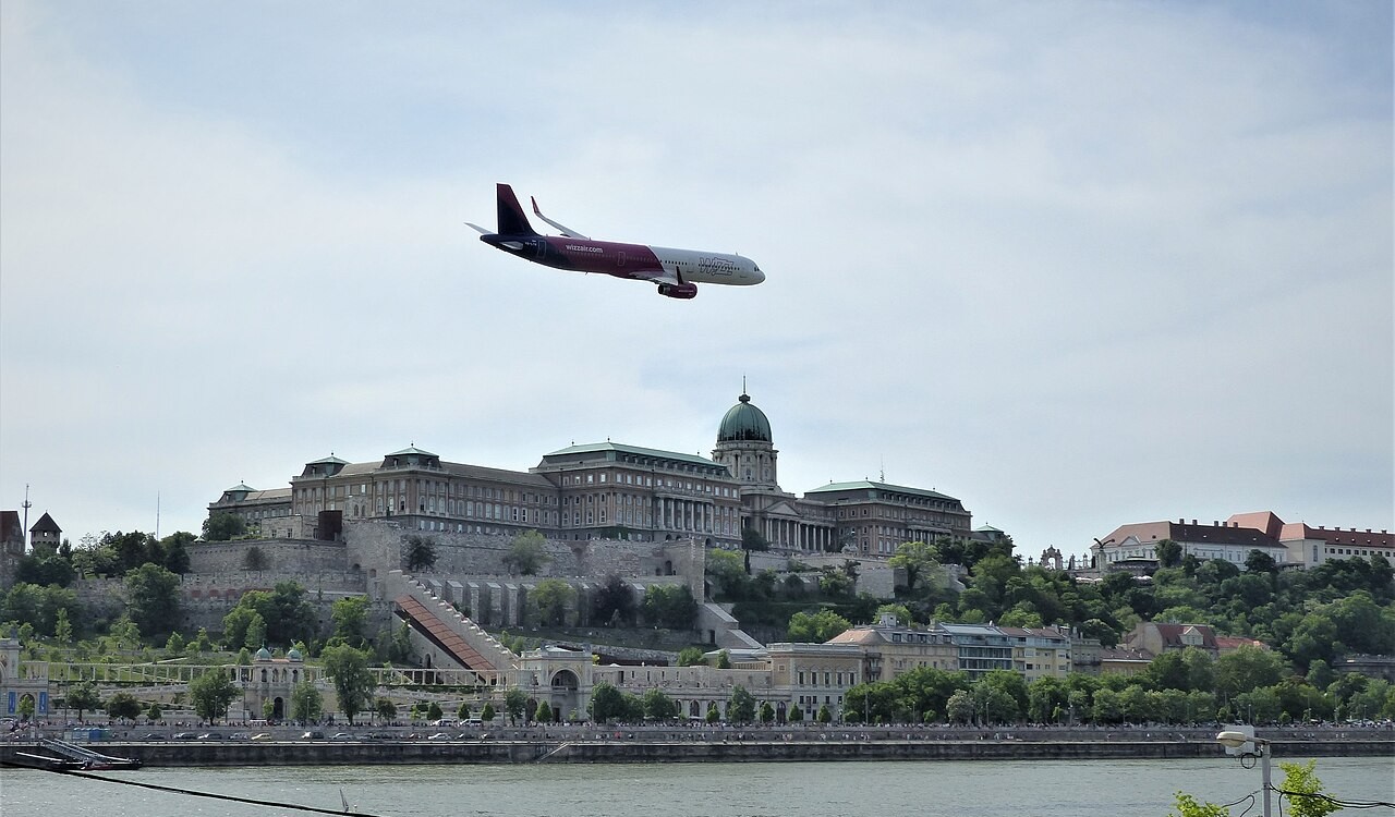 A Wizz Air aircraft flying over a river next to a historic building.
