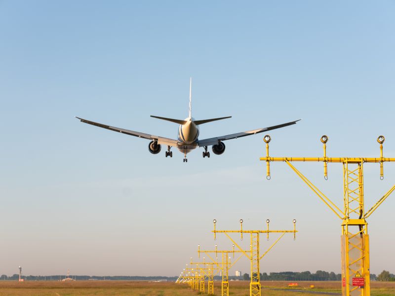 Aircraft landing on a runway at Amsterdam Schiphol Airport with the control tower visible in the distance