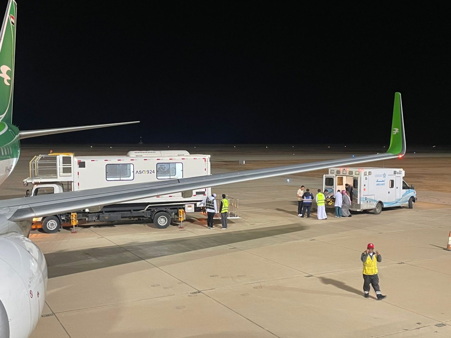 Ground crew and medical personnel in apron area transporting a patient on a stretcher into an ambulance.