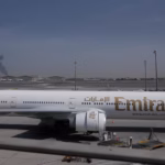 A plume of smoke caused by an Iranian strike is visible behind an Emirates plane parked at Dubai international airport on Sunday