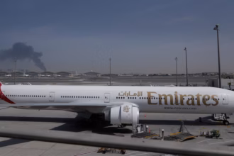A plume of smoke caused by an Iranian strike is visible behind an Emirates plane parked at Dubai international airport on Sunday