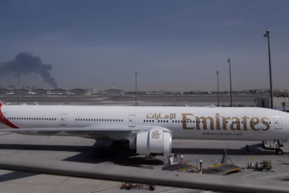 A plume of smoke caused by an Iranian strike is visible behind an Emirates plane parked at Dubai international airport on Sunday