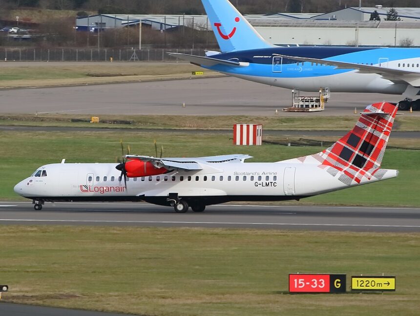 A Loganair ATR 72-600 turboprop aircraft, featuring its signature red-and-black tartan tail, taxies along an airport runway. In the background, the blue tail of a TUI Boeing 787 Dreamliner is visible