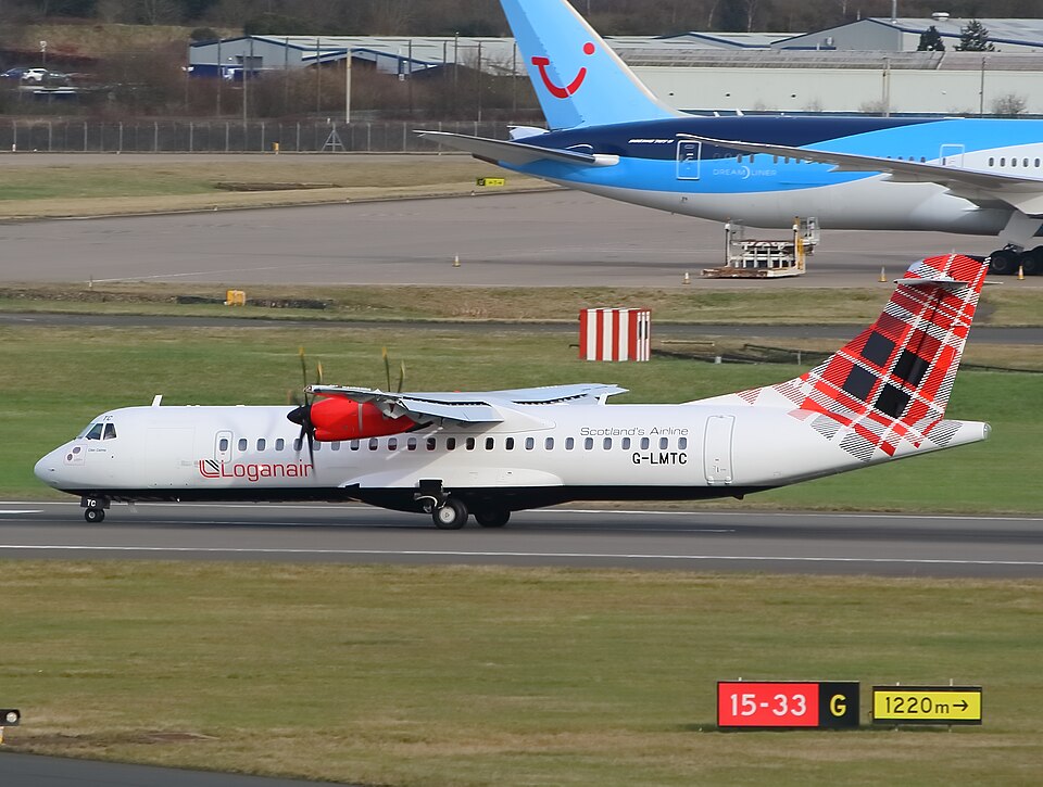 A Loganair ATR 72-600 turboprop aircraft, featuring its signature red-and-black tartan tail, taxies along an airport runway. In the background, the blue tail of a TUI Boeing 787 Dreamliner is visible