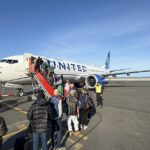 Low-angle shot of passengers in outdoor gear boarding a United Airlines Boeing 737 MAX 8 on a sunny day at Nuuk Airport, Greenland
