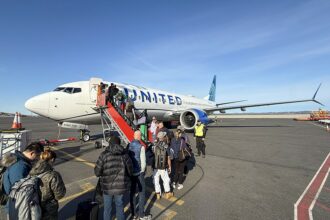Low-angle shot of passengers in outdoor gear boarding a United Airlines Boeing 737 MAX 8 on a sunny day at Nuuk Airport, Greenland