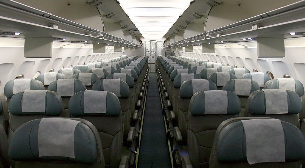 Interior of Jazeera Airways Airbus. Grey seats and overheat white lighting.