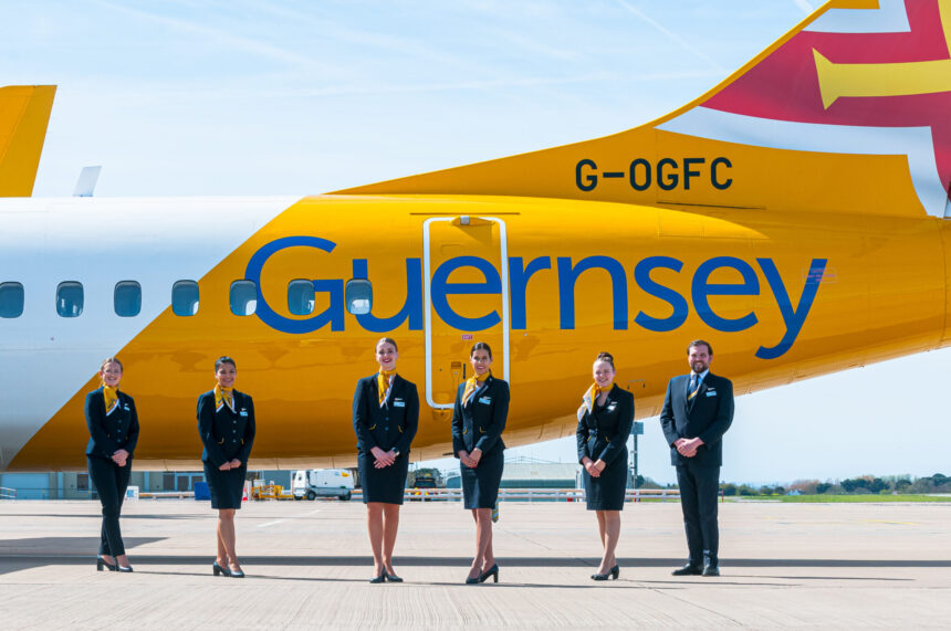 An image of a yellow and white aircraft on the ground with the word Guernsey on it and flight attendants standing in front of it.