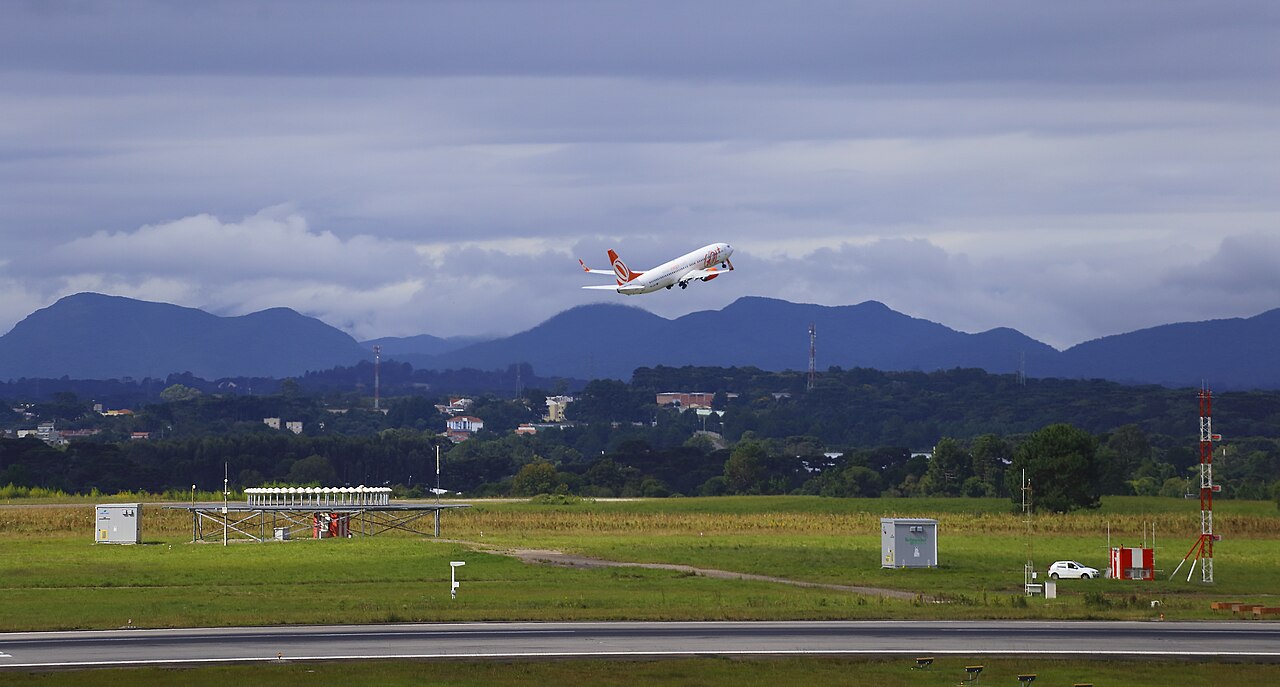 GOL aircraft takeoff, flying into the sky, mountains in background, grass in foreground.