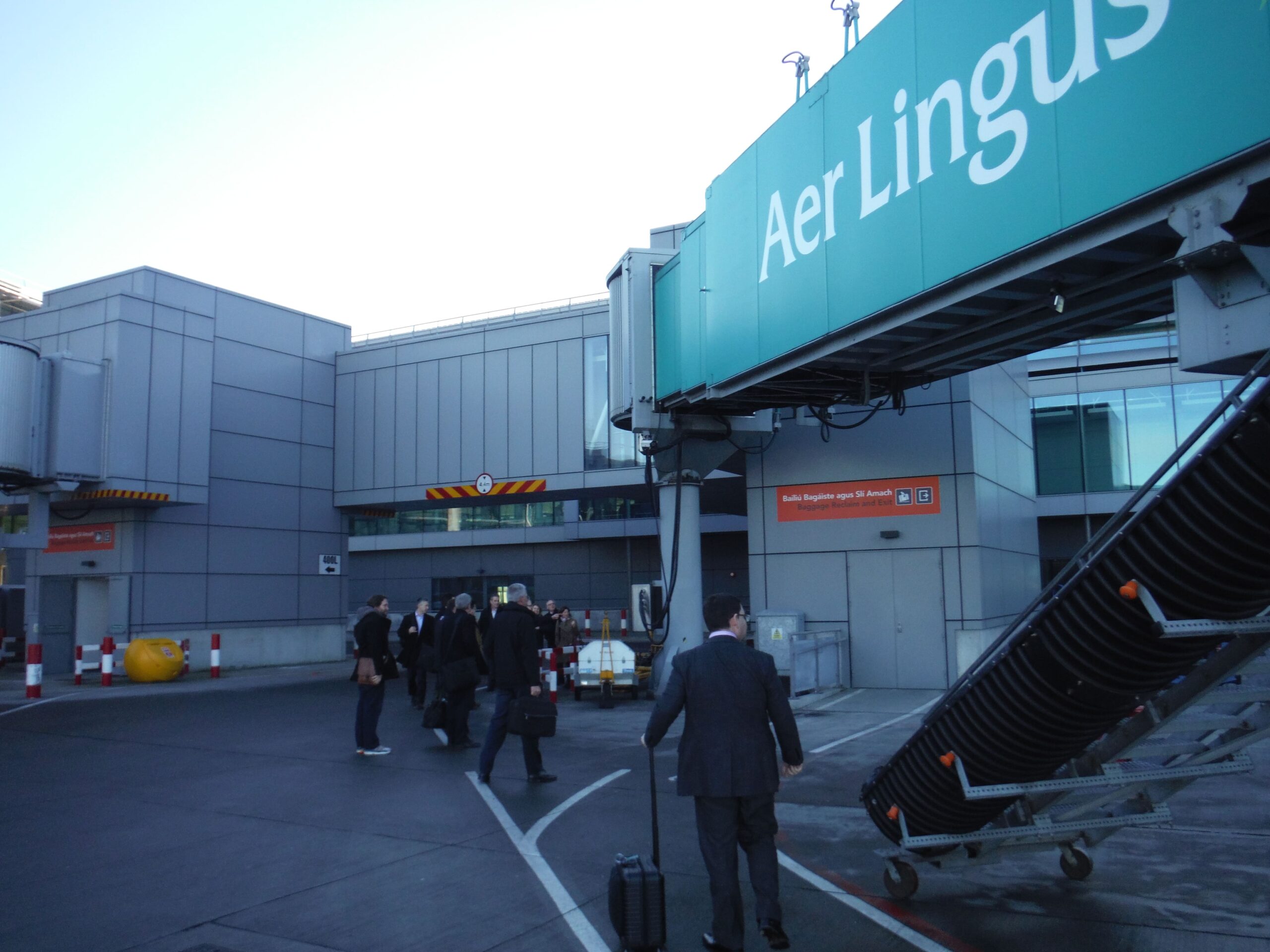 Passengers walking on the tarmac, close to an Aer Lingus banner outside a boarding gate.