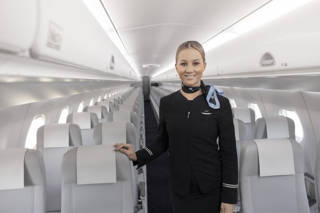 Interior of Embraer Finnair aircraft, crew member stood in aisle smiling.