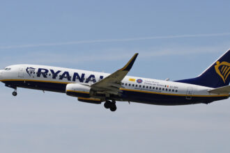 Ryanair Boeing 737 flying in blue sky; dispersing clouds in the background.