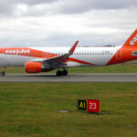A bright orange-and-white easyJet passenger jet taxis along a runway on a cloudy day.