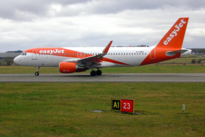 A bright orange-and-white easyJet passenger jet taxis along a runway on a cloudy day.