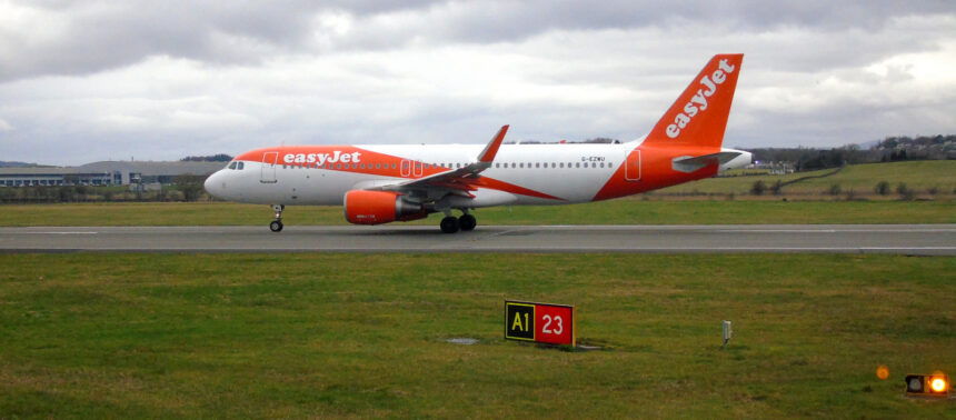 A bright orange-and-white easyJet passenger jet taxis along a runway on a cloudy day.