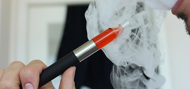 Man smoking an electronic cigarette, blowing smoke.