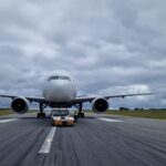 EirTrade Boeing 777-300ER on the runway amid grey clouds and grassy terrain towards the back of the image.