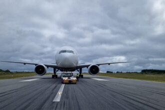 EirTrade Boeing 777-300ER on the runway amid grey clouds and grassy terrain towards the back of the image.