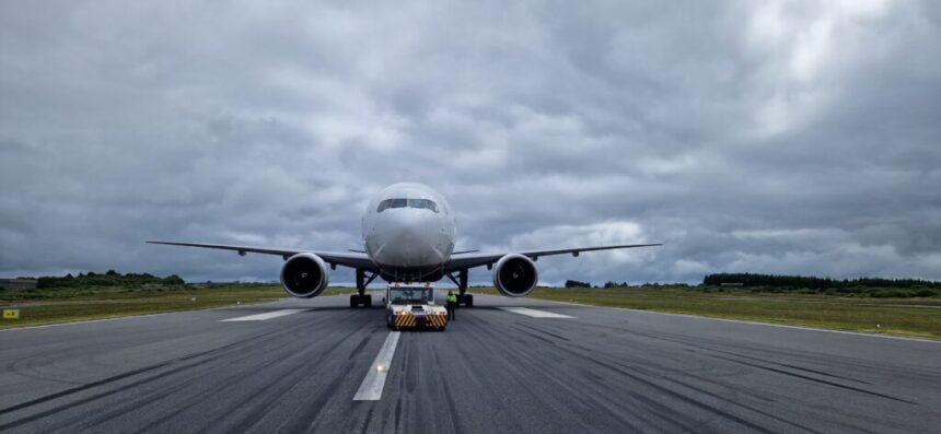 EirTrade Boeing 777-300ER on the runway amid grey clouds and grassy terrain towards the back of the image.