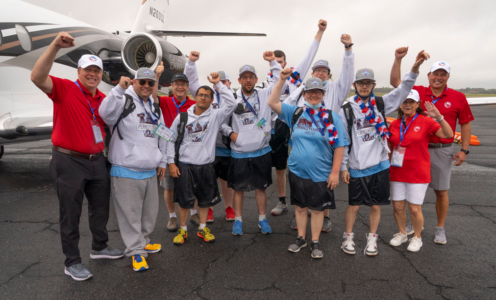 12 members of Special Olympics airlift with their fists in the air, stood in front of an aircraft.