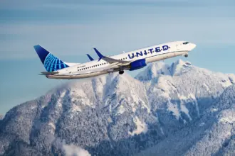 A United Airlines plane flying amid blue skies and a mountainous scenery below.