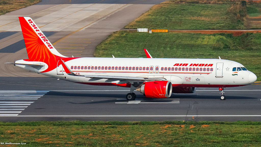 A white and red Air India Airbus A320neo taxis across a runway at an airport.